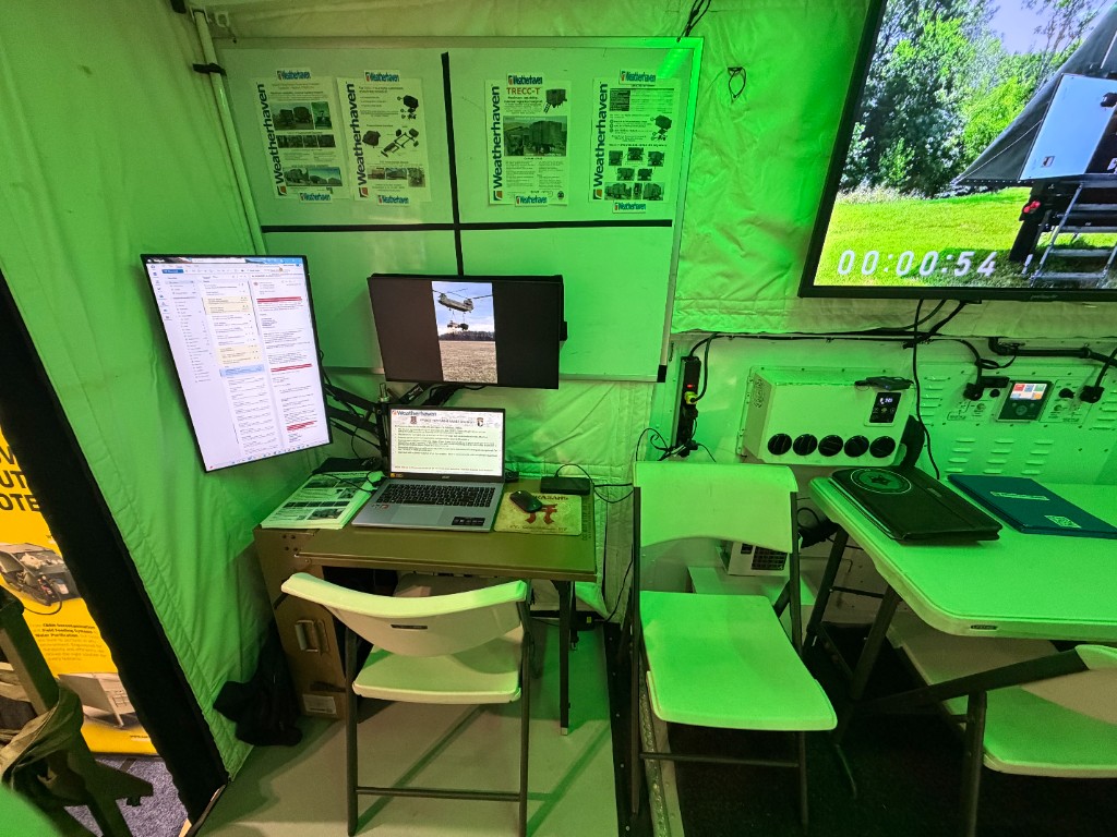 Weatherhaven partner booth at AUSA Huntsville with integrated R.E.C.O.N. workstation, dual monitors, and shelter posters in a tactical shelter environment